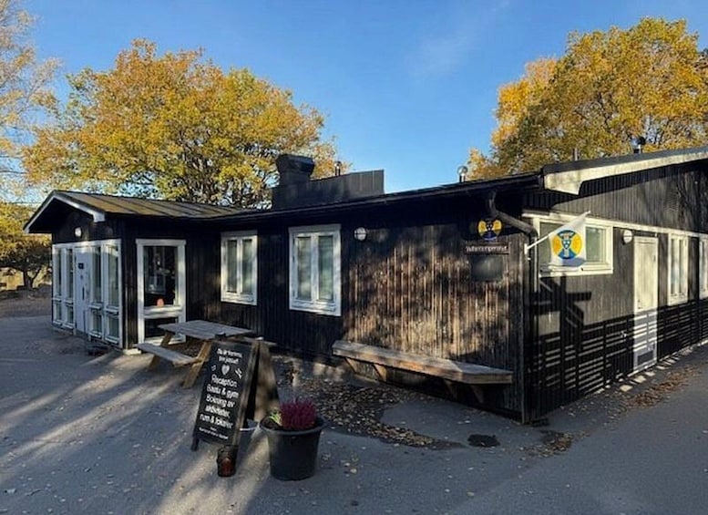 A rustic wooden building with a black exterior, white windows, and a signboard. 4