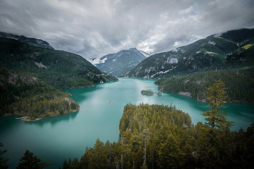 A turquoise lake surrounded by dense forests and mountains under a cloudy sky. 4