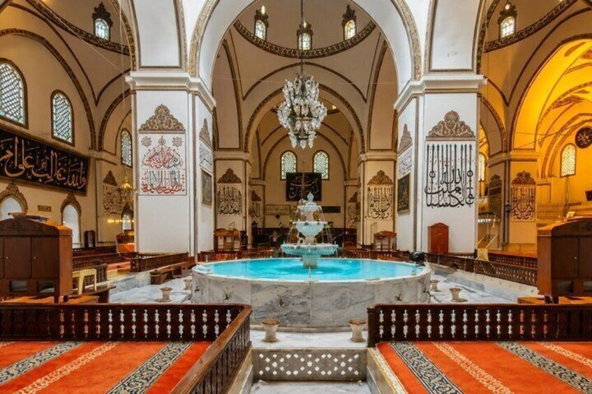 An ornate church interior with a central fountain, arched ceilings, and Arabic calligraphy. 1