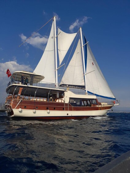 A sailing yacht with white sails and a red flag, docked at a pier. 1