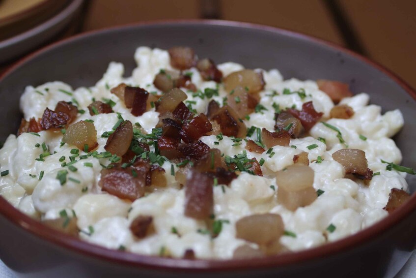 A bowl of creamy food with diced bacon and chopped herbs. 5