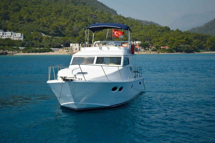 A white boat with a Turkish flag on a calm sea, surrounded by lush green hills and buildings. 4