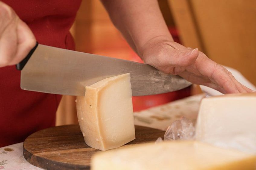 A person cutting a large block of cheese with a knife on a wooden board. 4
