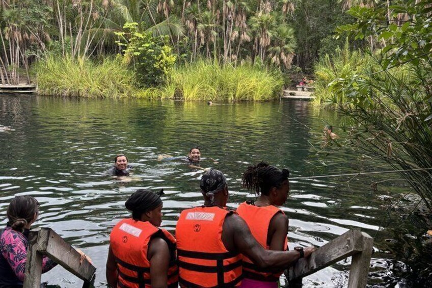 Un grupo de personas en un río, usando chalecos salvavidas, rodeadas de exuberante vegetación. 3