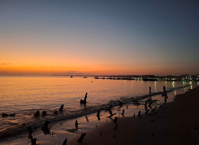 A sunset over a calm sea with a beach, boats, and a pier in the distance. 1
