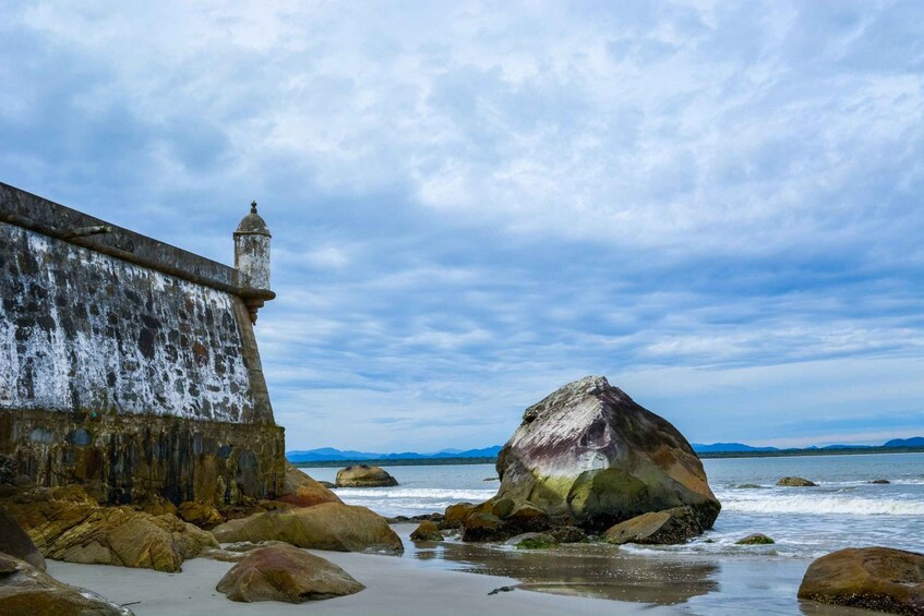 A coastal scene with a weathered lighthouse, large boulders, and a calm sea under a cloudy sky. 5