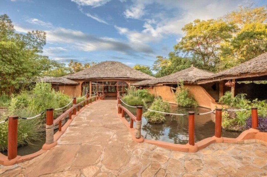 A stone bridge leading to thatched-roof structures surrounded by greenery. 2