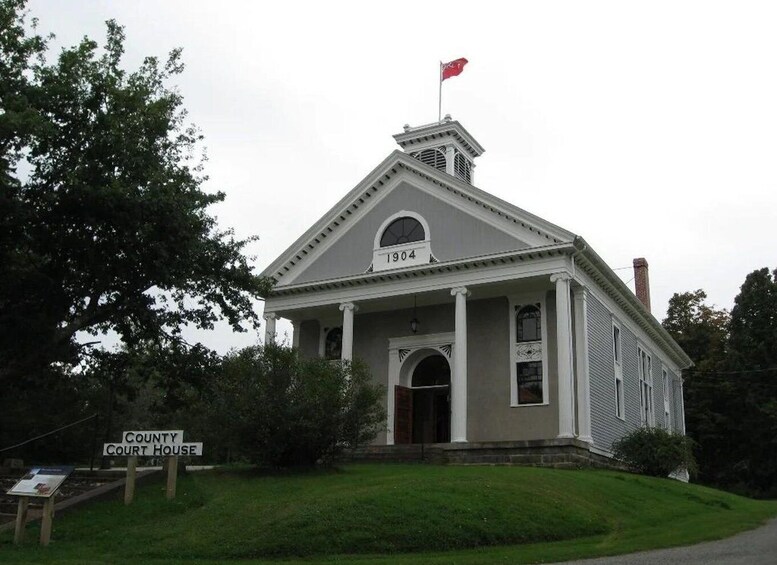 A courthouse with a flag on top, a year marker, and a sign indicating its purpose. 1