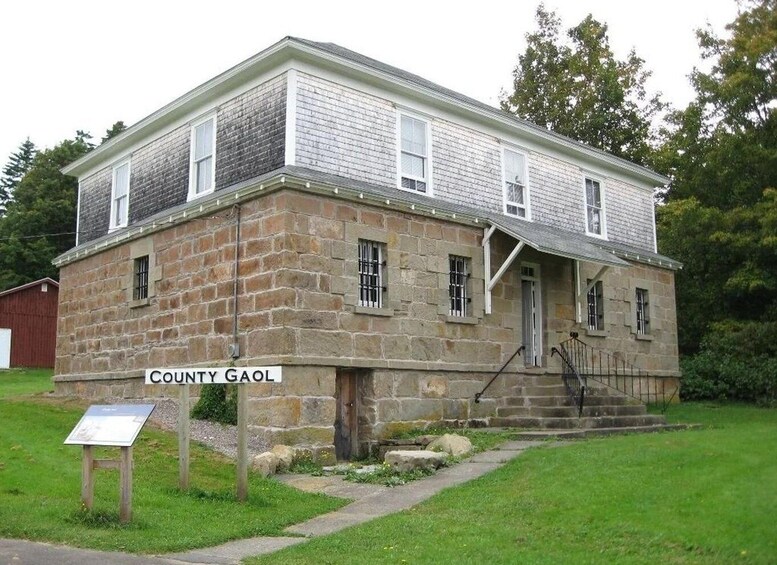 A two-story stone building with a sign reading 'County Gaol' in front. 3