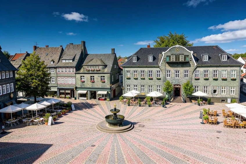 A cobblestone square with a fountain, surrounded by traditional European buildings with outdoor seating. 1