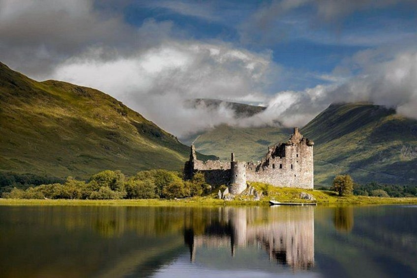 A historic castle on a lake surrounded by hills. 1