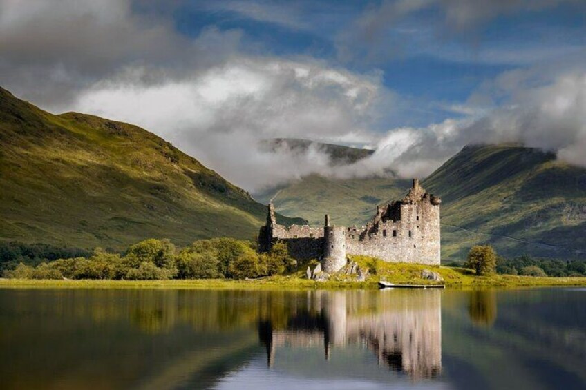 A historic castle by a calm lake with surrounding hills. 1