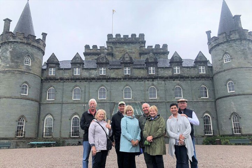 A group of people standing in front of a large, historic castle with multiple towers and arched windows. 2