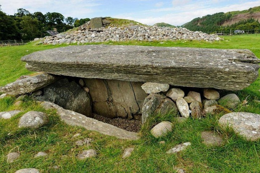 A stone structure with a flat top and a circular base, surrounded by grass and rocks. 3