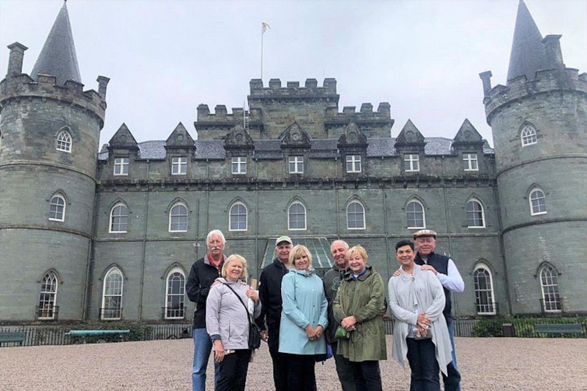 A group of people standing in front of a large, historic castle with multiple towers and arched windows. 5