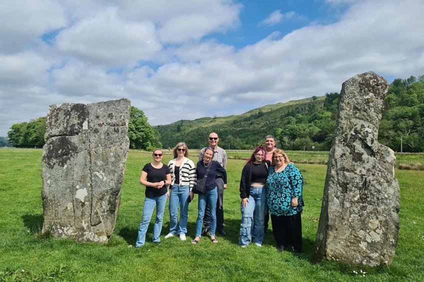 A group of people standing between two large stone structures in a grassy field with hills in the background. 4