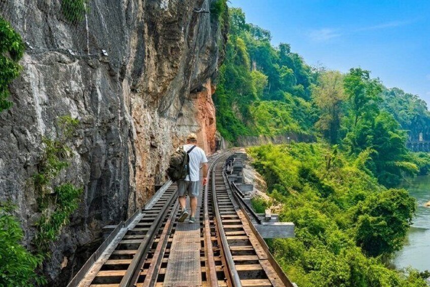 A person standing on a railway track with a steep cliff on one side and a river on the other. 5