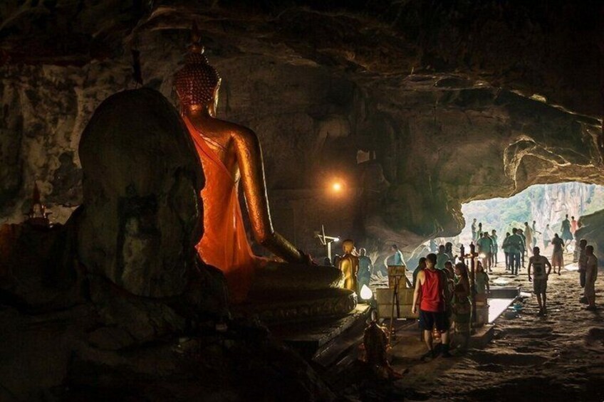A large Buddha statue in a cave with a crowd of people around it. 3