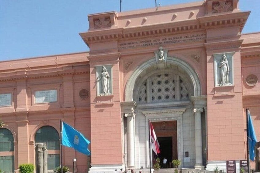 A pink building with a large arched entrance, statues, and flags. 4