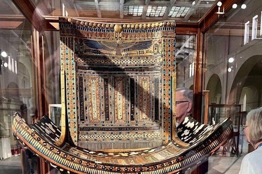 An ornate, intricately decorated chair with a high backrest and a curved seat, displayed in a museum setting. 2