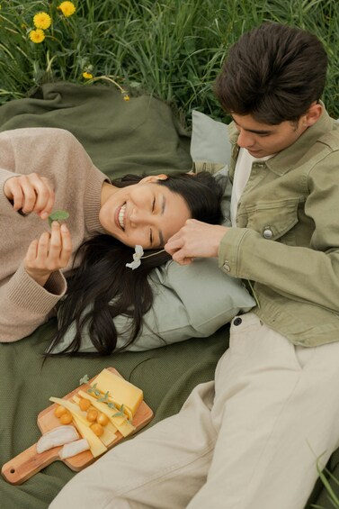 Two people lying on a blanket outdoors with a cheese board nearby. 5