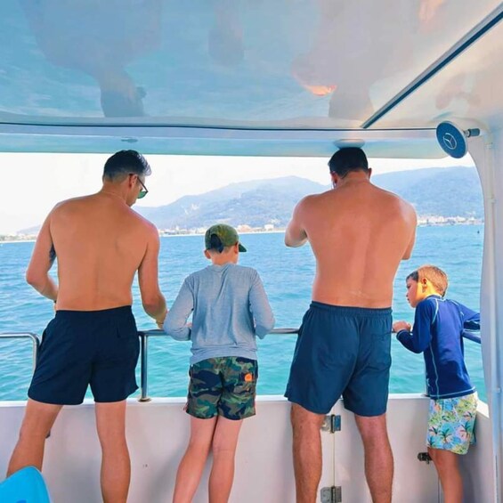 Three adults and two children on a boat, looking out at a body of water with distant land and mountains. 2