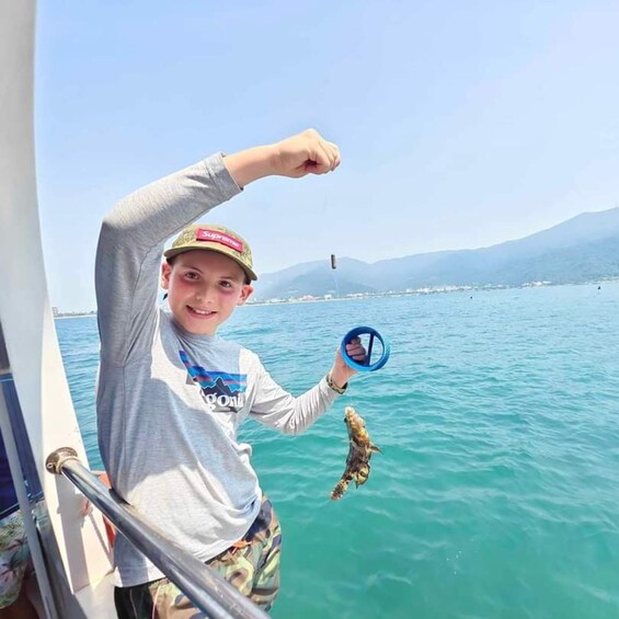 A person holding a fish on a boat with a mountainous landscape in the background. 4