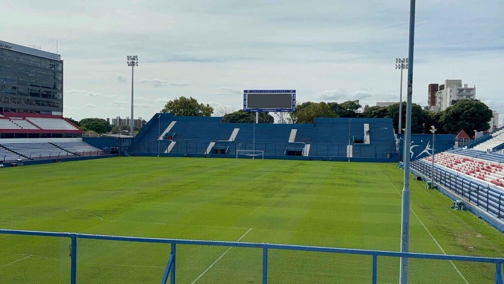 A sports stadium with blue seating, a green field, and a large scoreboard. 3