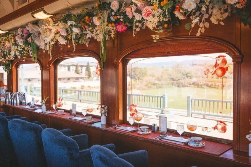 Una carrozza ristorante con tavoli apparecchiati, decorata con fiori e lanterne rosse, con vista su un paesaggio pittoresco. 1