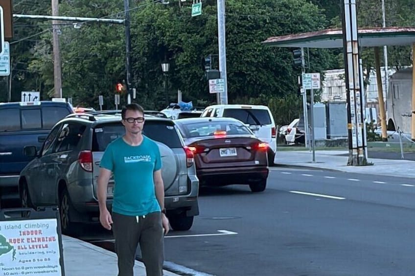A person standing on a sidewalk, a road with cars, and a gas station in the background. 1