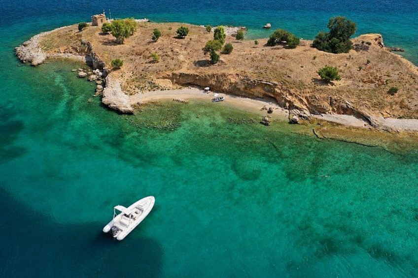 A small island with clear turquoise waters, a boat anchored near the shore, and rocky terrain with sparse vegetation. 1