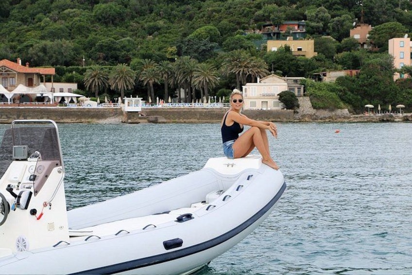 A person sitting on a white inflatable boat on calm water, with a coastal town and greenery in the background. 2