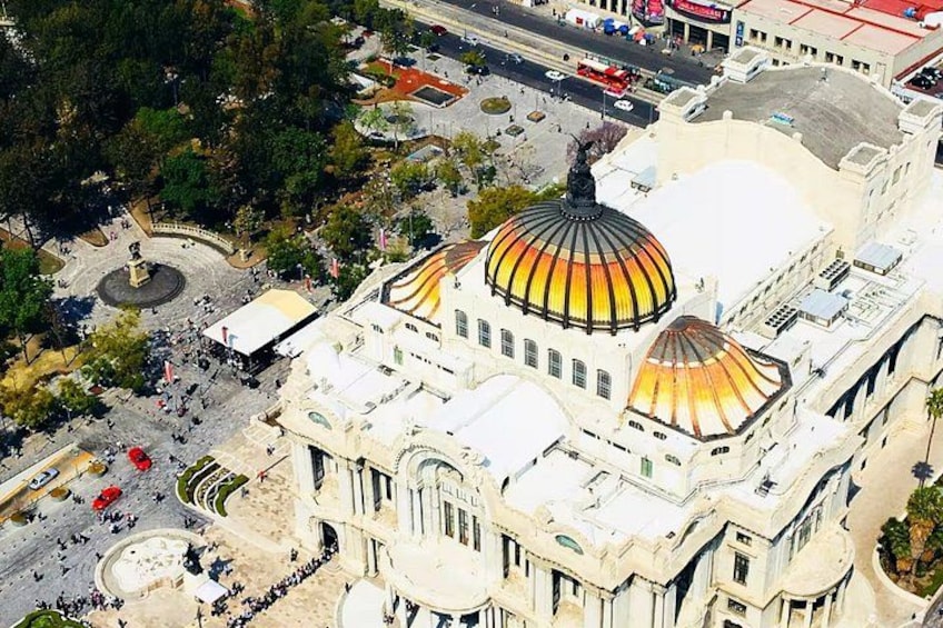 An aerial view of a large building with a prominent dome, surrounded by trees and a plaza with people. 3