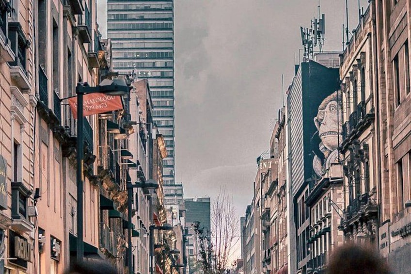A city street lined with historic buildings, a tall modern skyscraper, and a large mural on one building. 5