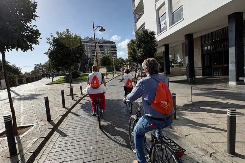 Een persoon fietst over een verhard pad, een andere persoon loopt, en er staat een gebouw op de achtergrond. 2