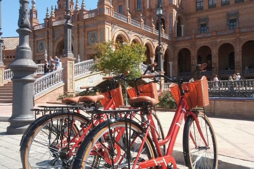 Een rode fiets met mandjes geparkeerd voor een historisch gebouw met bogen en een fontein. 3