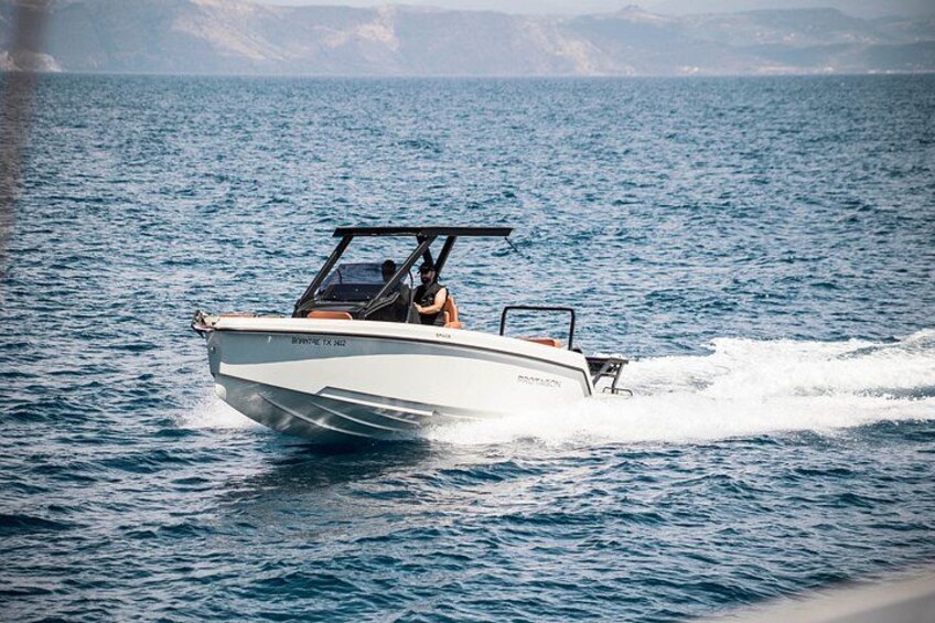 Ein weißes Schnellboot mit einer Person am Steuer bewegt sich über ruhiges Wasser, im Hintergrund eine Küstenlinie. 1