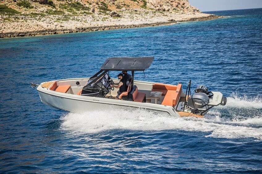 A motorboat on a clear blue sea with rocky coastline in the background. 1