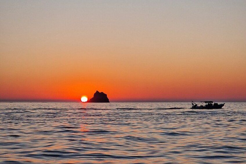 Ein Sonnenuntergang über dem Meer mit einem Boot und einer Felsformation. 5