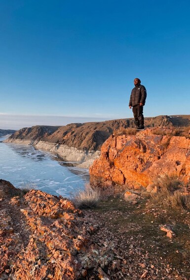 A person standing on a rocky outcrop overlooking a frozen body of water. 4