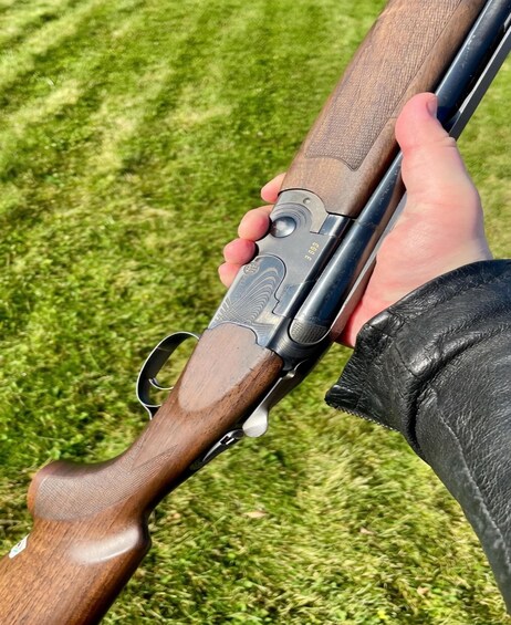 A person holding a shotgun with a wooden stock and metal barrel, standing on grass. 5