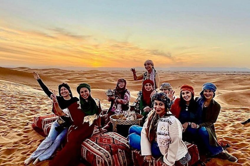 A group of people sitting on a camel in a desert with sand dunes and a sunset in the background. 3