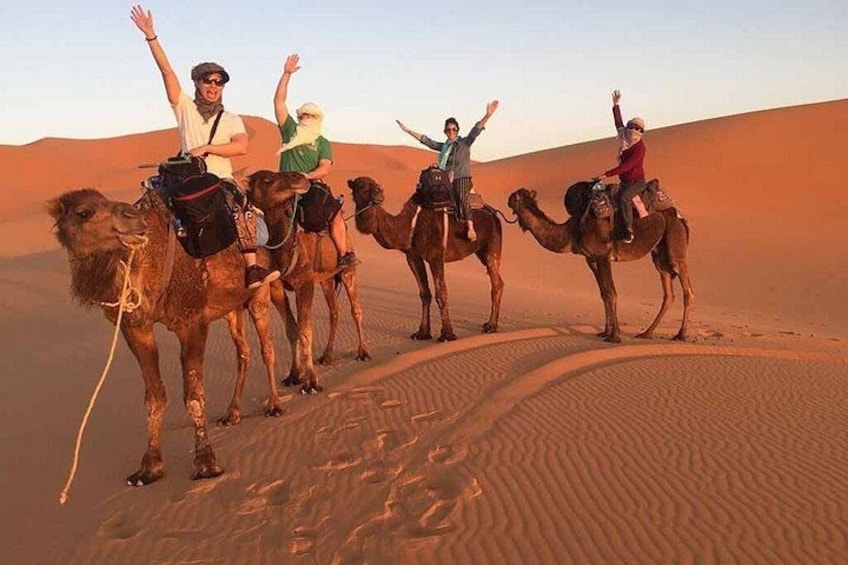 A group of people riding camels across a desert landscape with sand dunes. 1