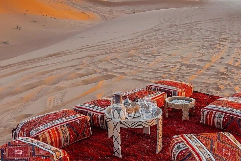 A desert scene with a table set for a meal, surrounded by colorful cushions and a red carpet. 2