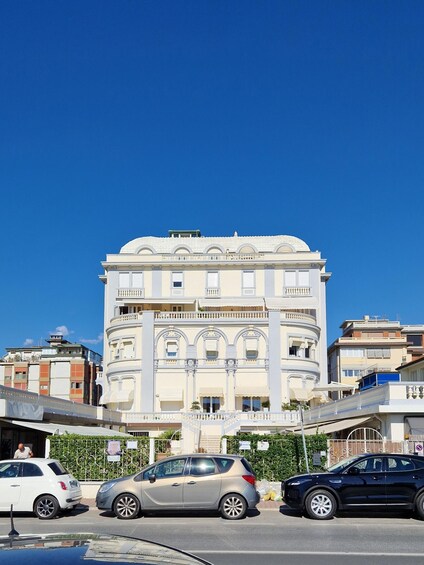 A multi-story building with classical architecture, including columns and a dome, in an urban setting with parked cars. 2