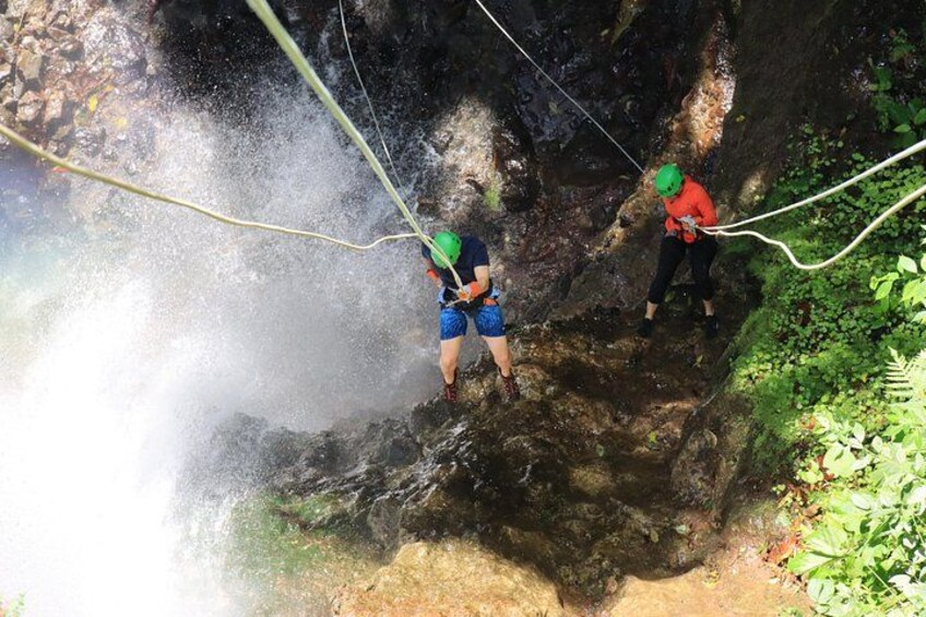 Dos personas descendiendo en rápel por un risco rocoso mientras el agua salpica a su alrededor. 4