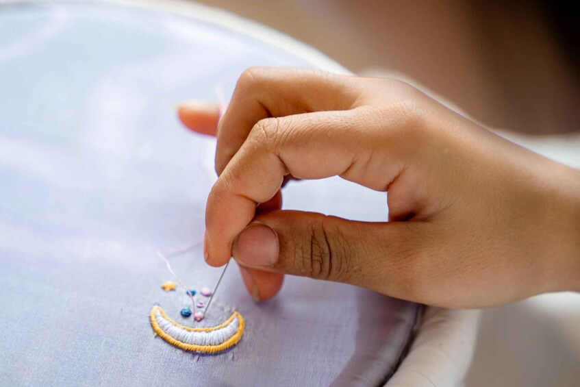 A hand embroidering a pattern on fabric. 1