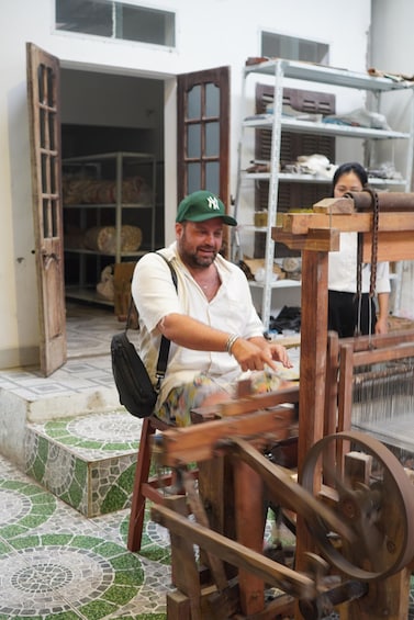 A person operating a wooden loom outdoors. 3
