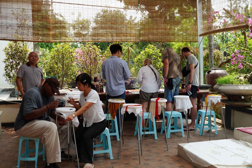 People dining outdoors with tables and chairs, surrounded by lush greenery and flowering plants. 2