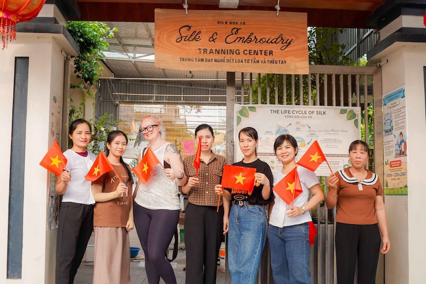 A group of people holding Vietnamese flags in front of a silk embroidery training center. 5